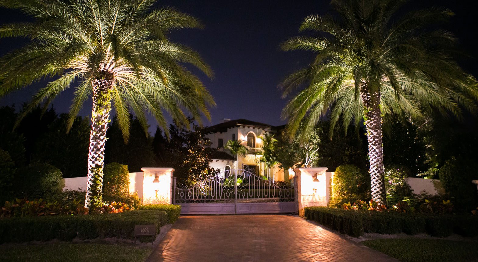 Modern Florida home with expansive glass walls illuminated by architectural landscape lighting and warm interior glow at dusk.